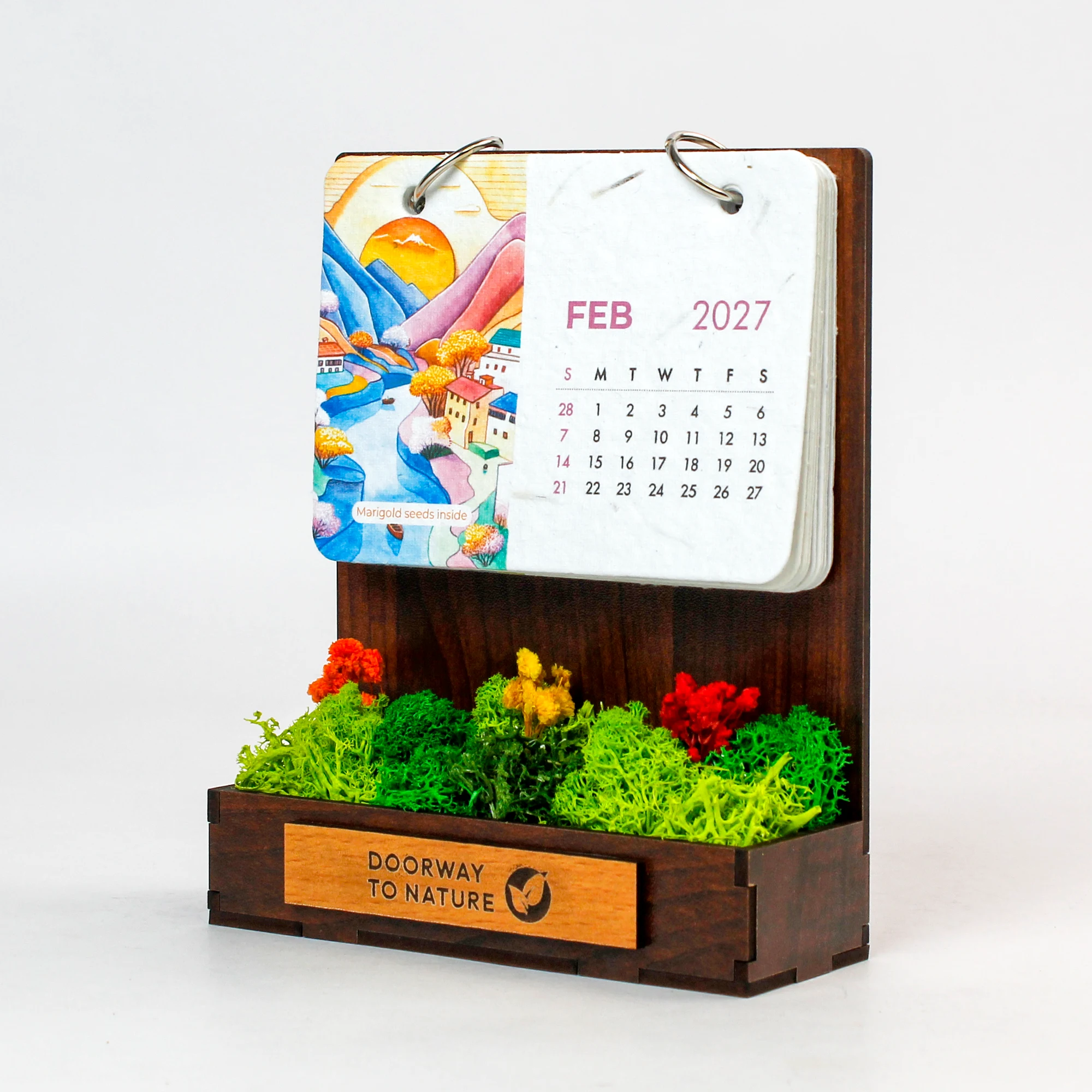 The Forest Garden calendar from an angle: February 2027 on two rings above a bed of preserved flowers and moss